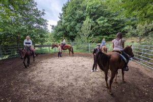 Persone a cavallo in un maneggio circondato da alberi.